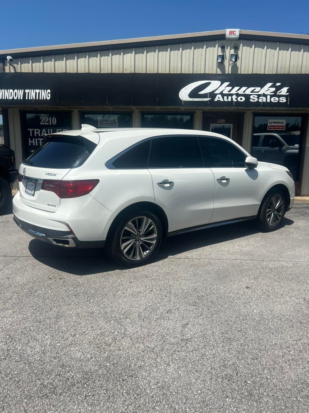 White Acura SUV parked in front of Chuck's Auto Sales building with tinted windows on a sunny day.