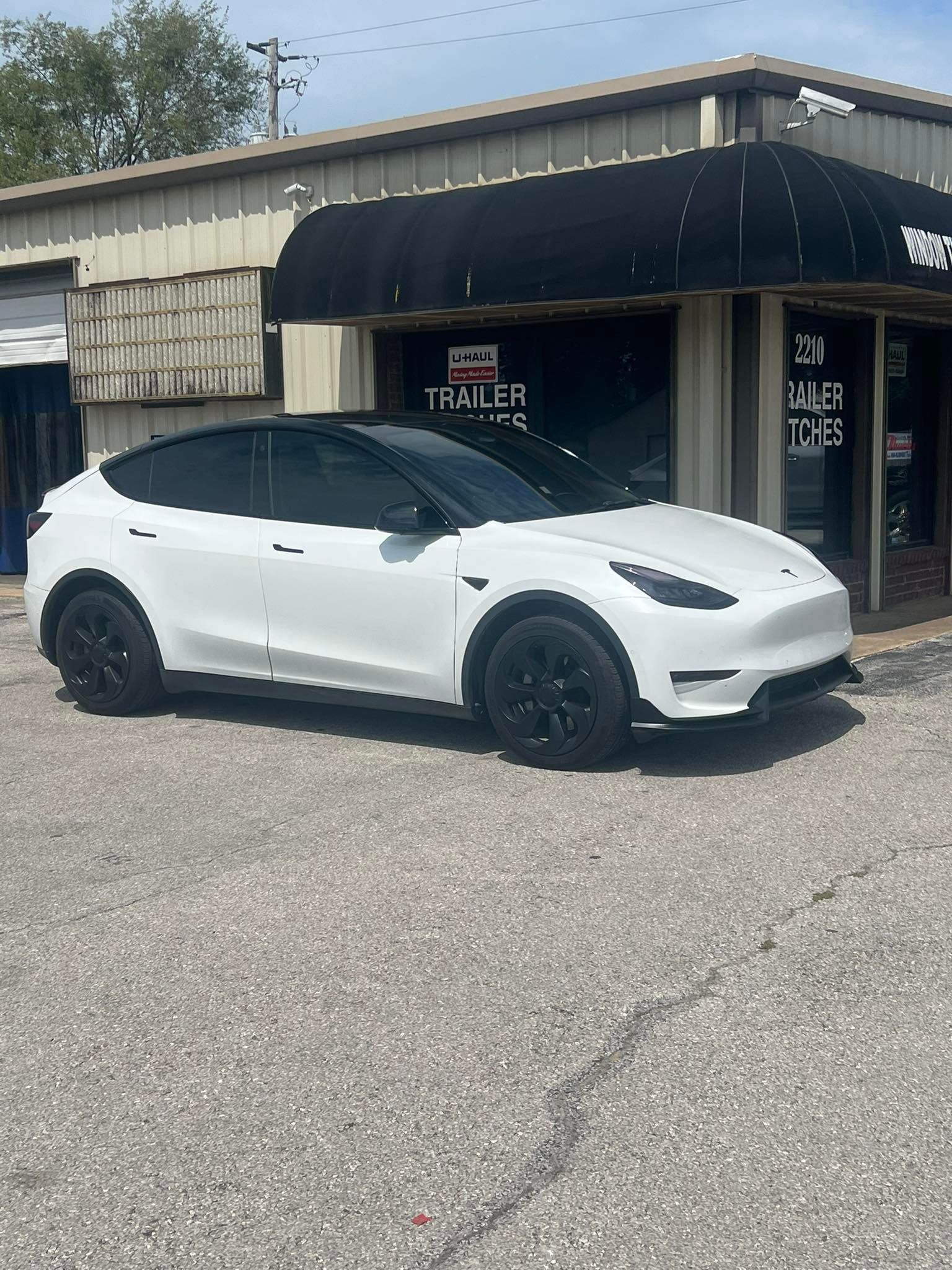White Tesla Model Y parked in front of a building with a black awning. Black wheels and trim.