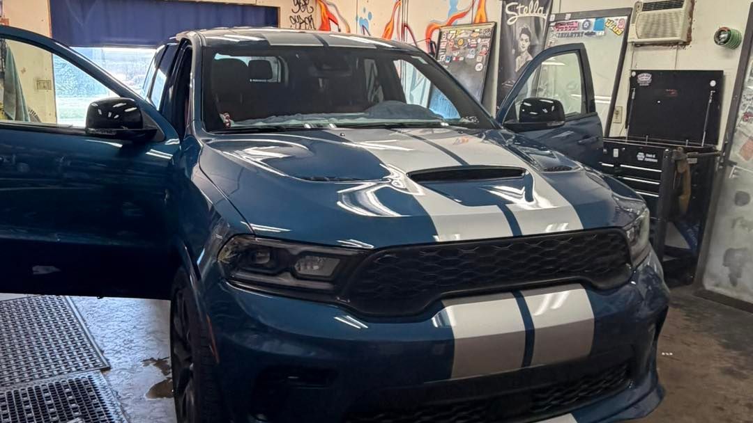 Blue Dodge Durango with white racing stripes; doors open, in a garage setting.