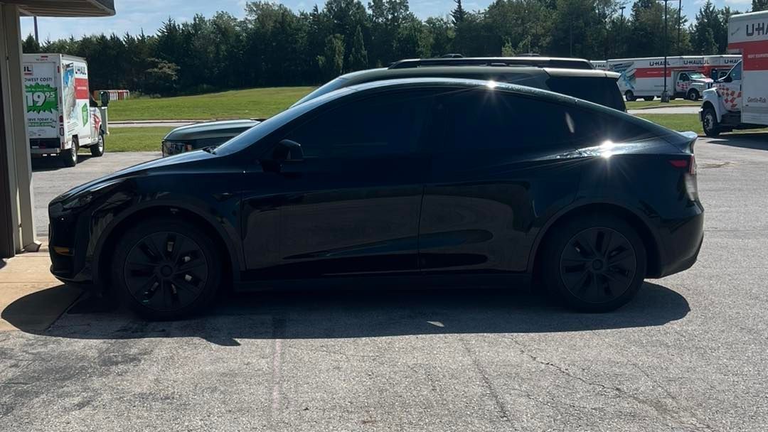 Black Tesla car parked near moving trucks.