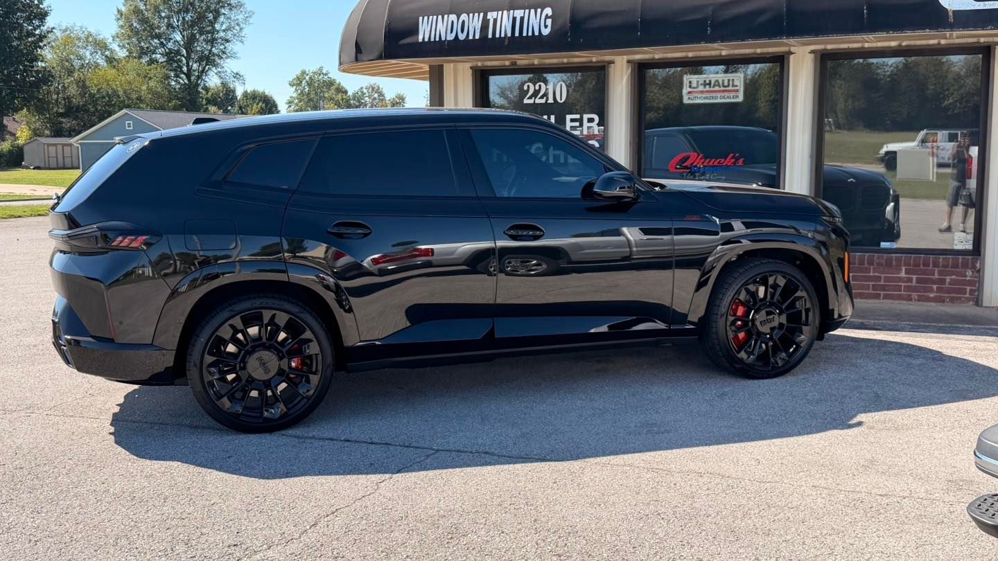Black SUV with tinted windows parked outside a window tinting shop.