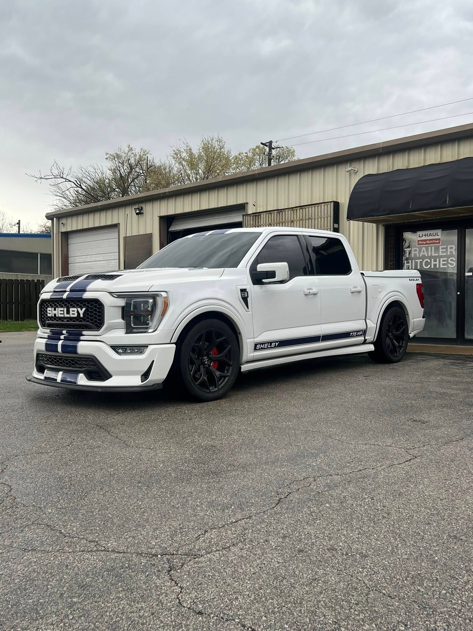 White Ford F-150 truck with black racing stripes parked outside a building on an overcast day.