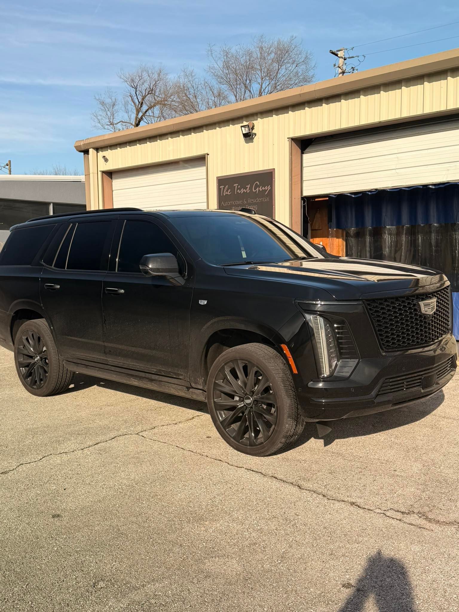 Black Cadillac Escalade parked outside a light-colored building. The car has black rims and tinted windows.