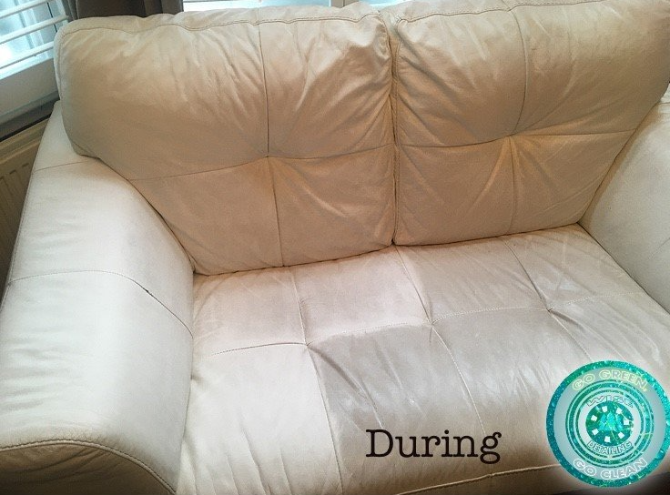 A white leather couch is sitting in front of a window.