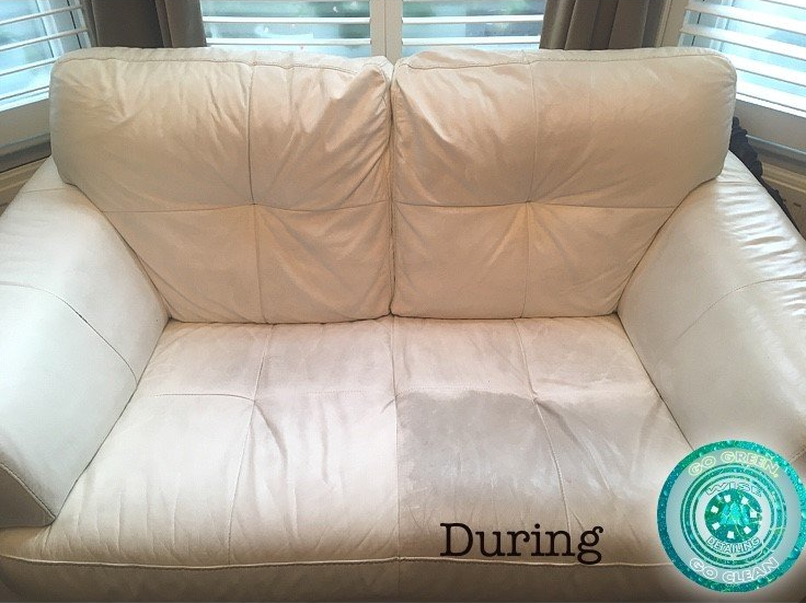A white leather couch is sitting in front of a window.