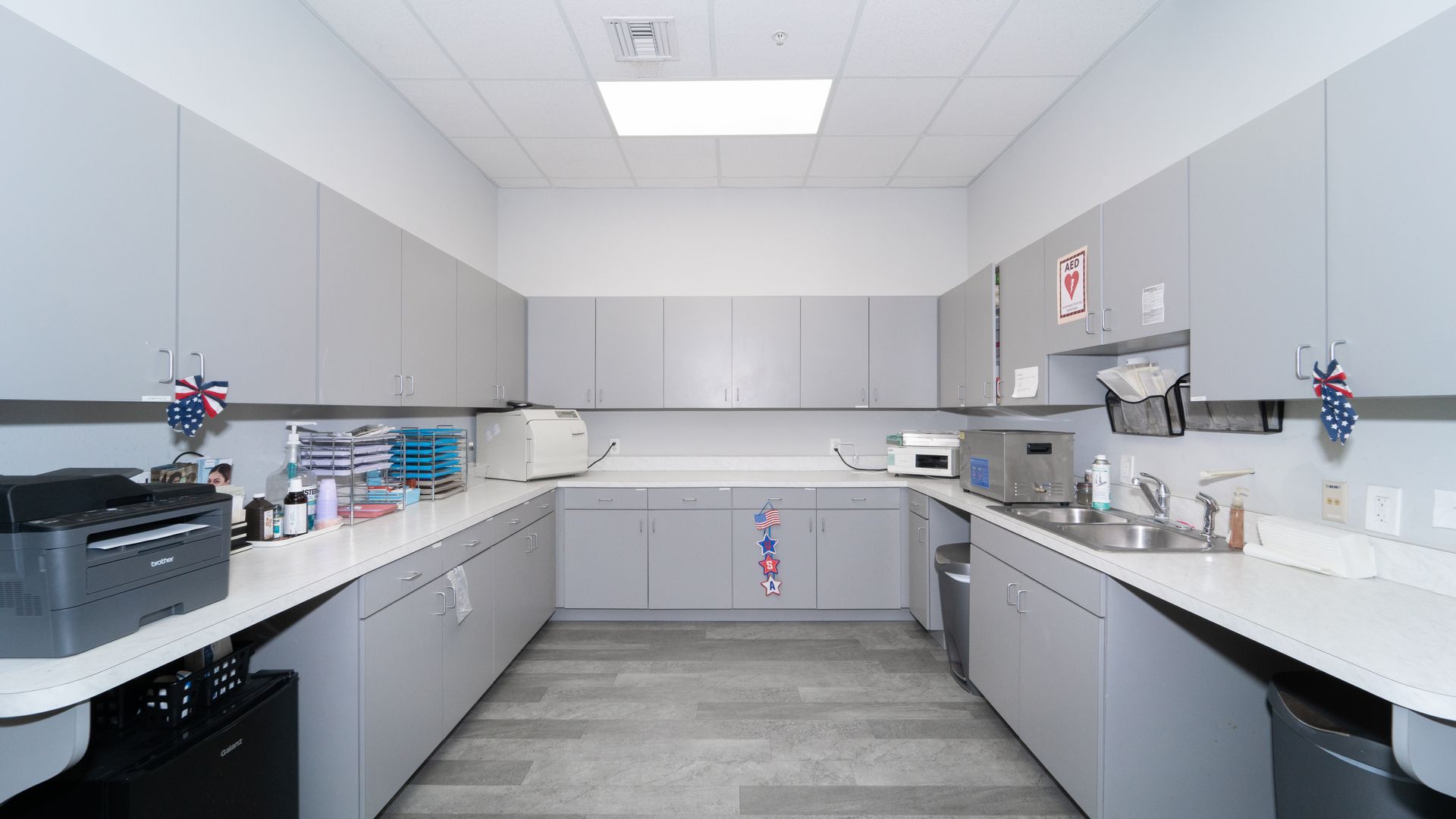 A kitchen with gray cabinets , white counter tops , a sink , and a printer.