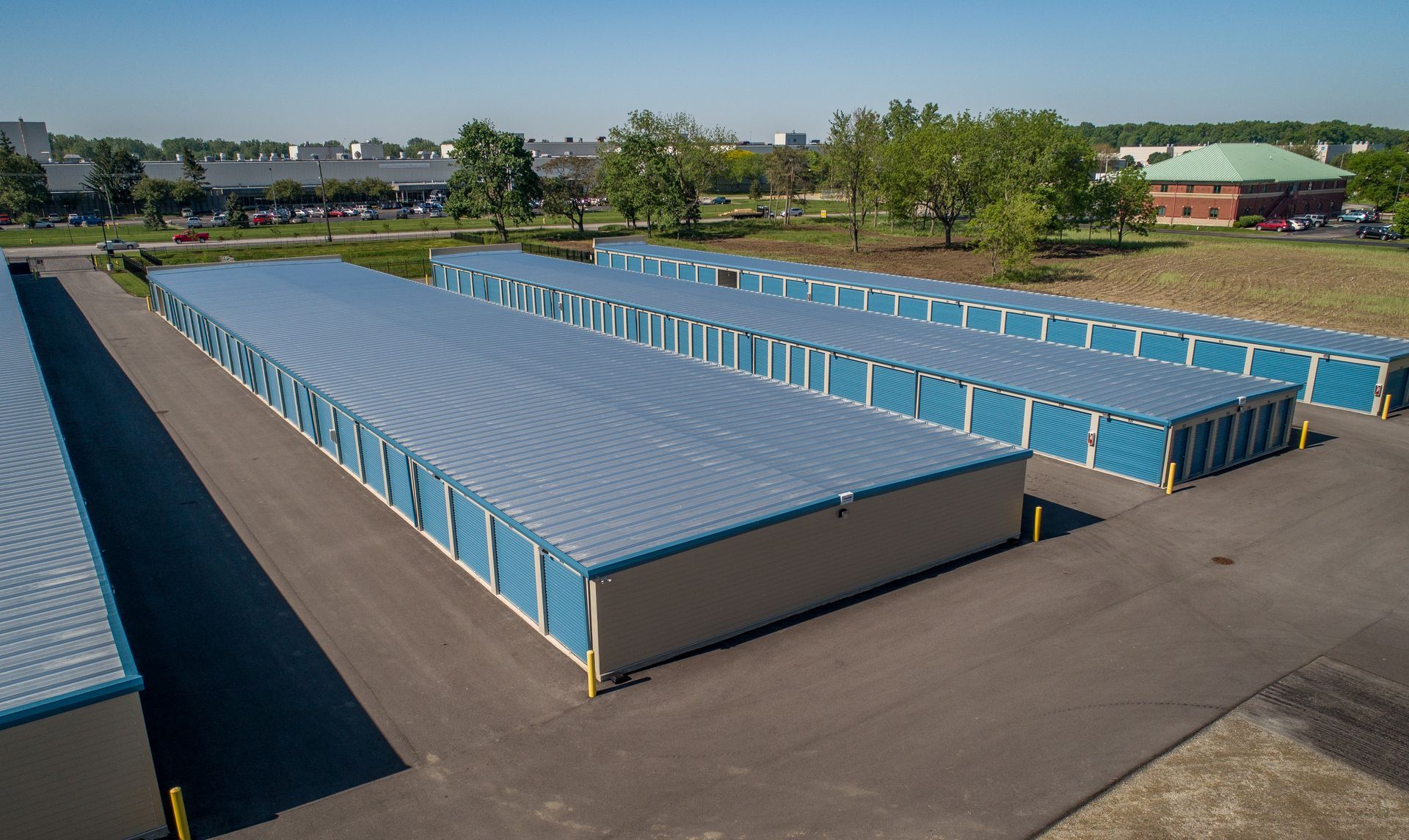 Exterior of storage units with cars parked in front, trees in the background, and a cloudy sky.