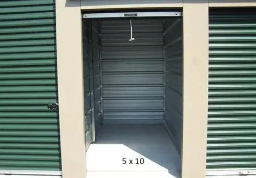 Interior of a 5x10 storage unit, showing metal walls, a concrete floor, and an open door.