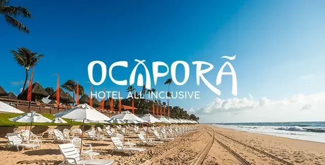 Cena de praia no Ocaporã Hotel All Inclusive com espreguiçadeiras brancas, guarda-sóis e céu azul.