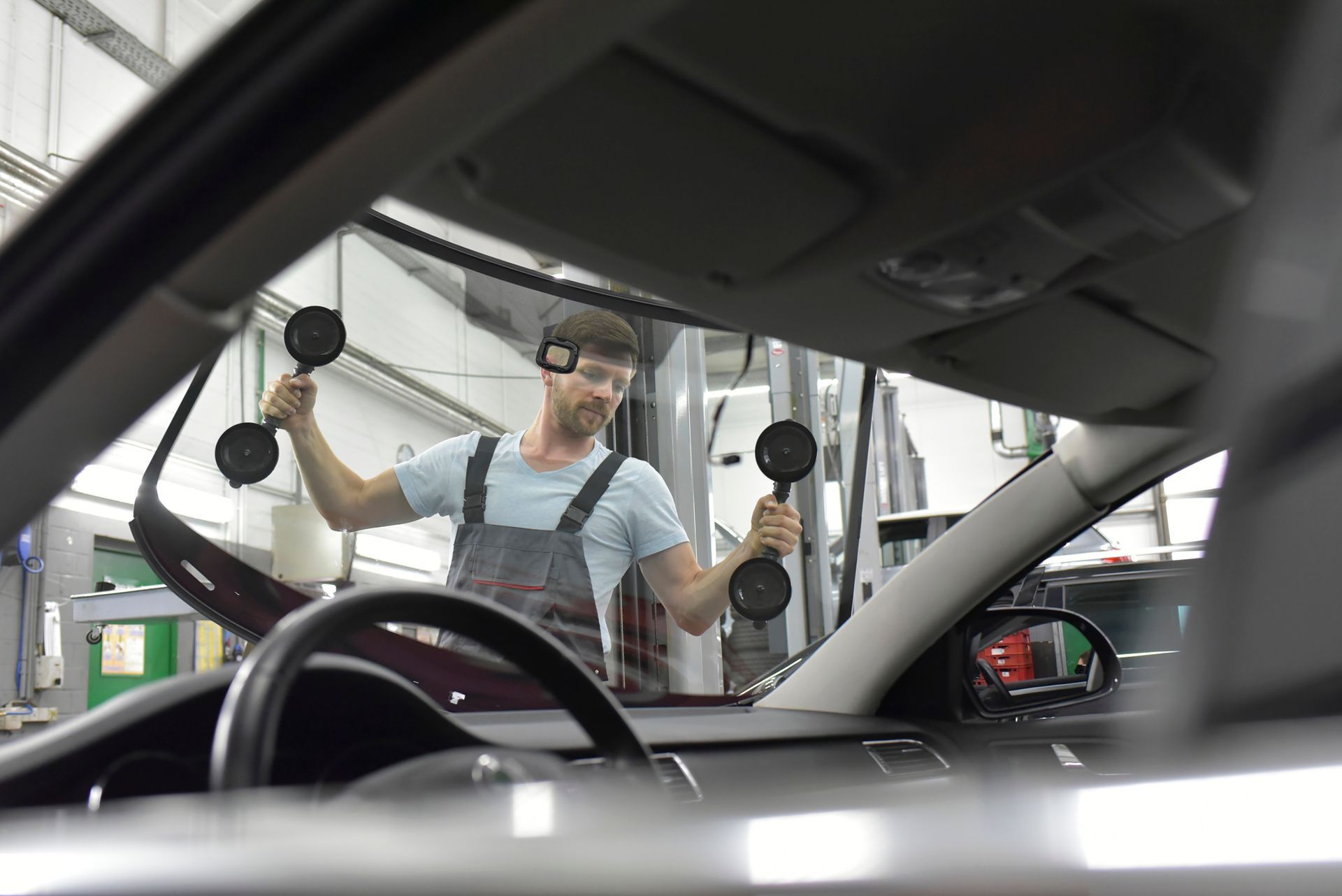 Un meccanico utilizza delle ventose per installare un parabrezza all'interno di un'auto in un garage.