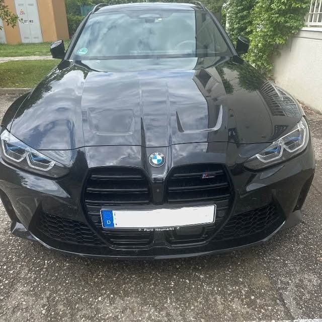 Un'auto BMW nera parcheggiata davanti a un edificio. La parte anteriore dell'auto è visibile con la targa e il logo BMW.