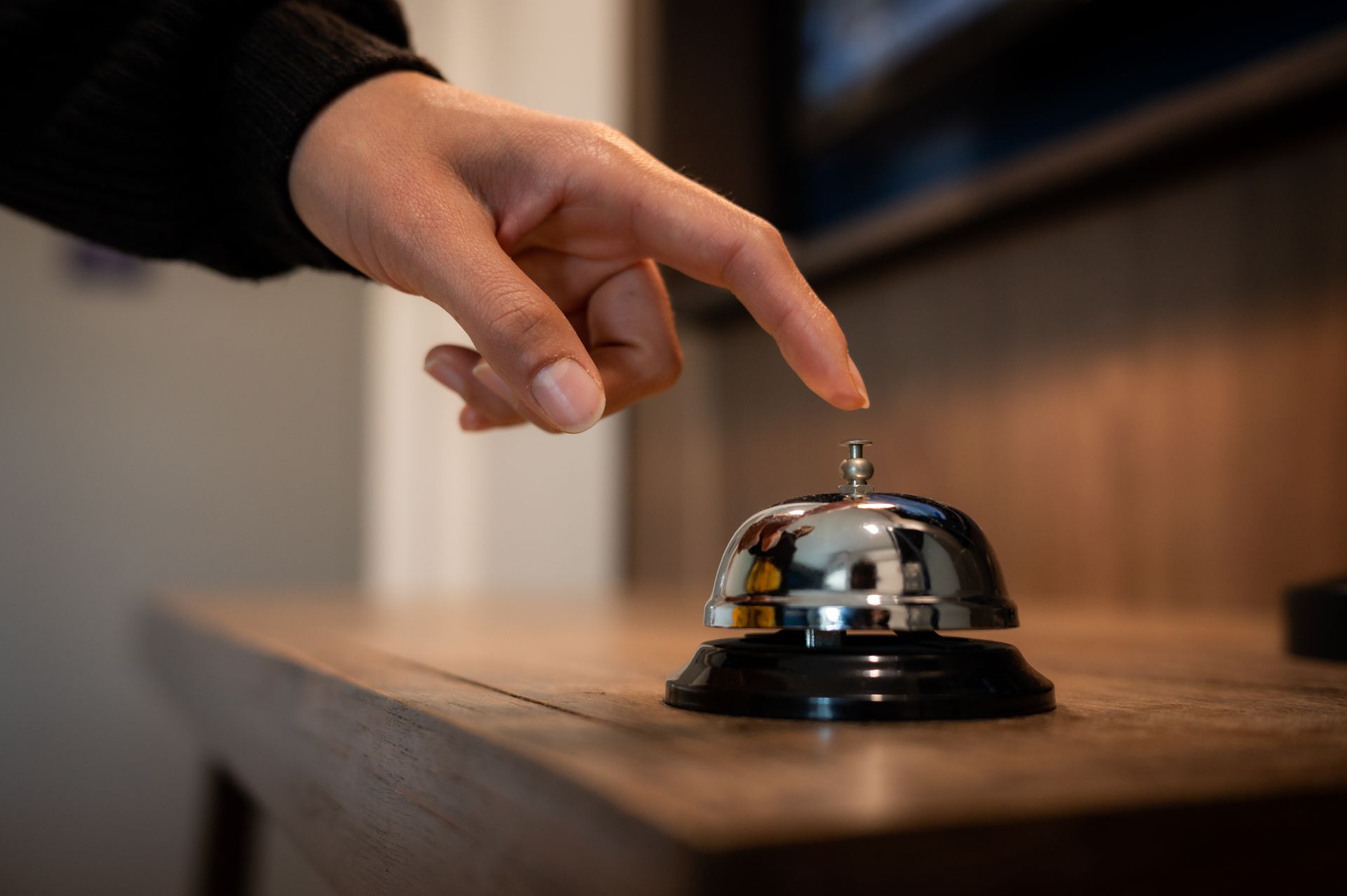 Il dito della persona preme un campanello d'argento su una superficie di legno, pronto a dare il segnale di servizio.