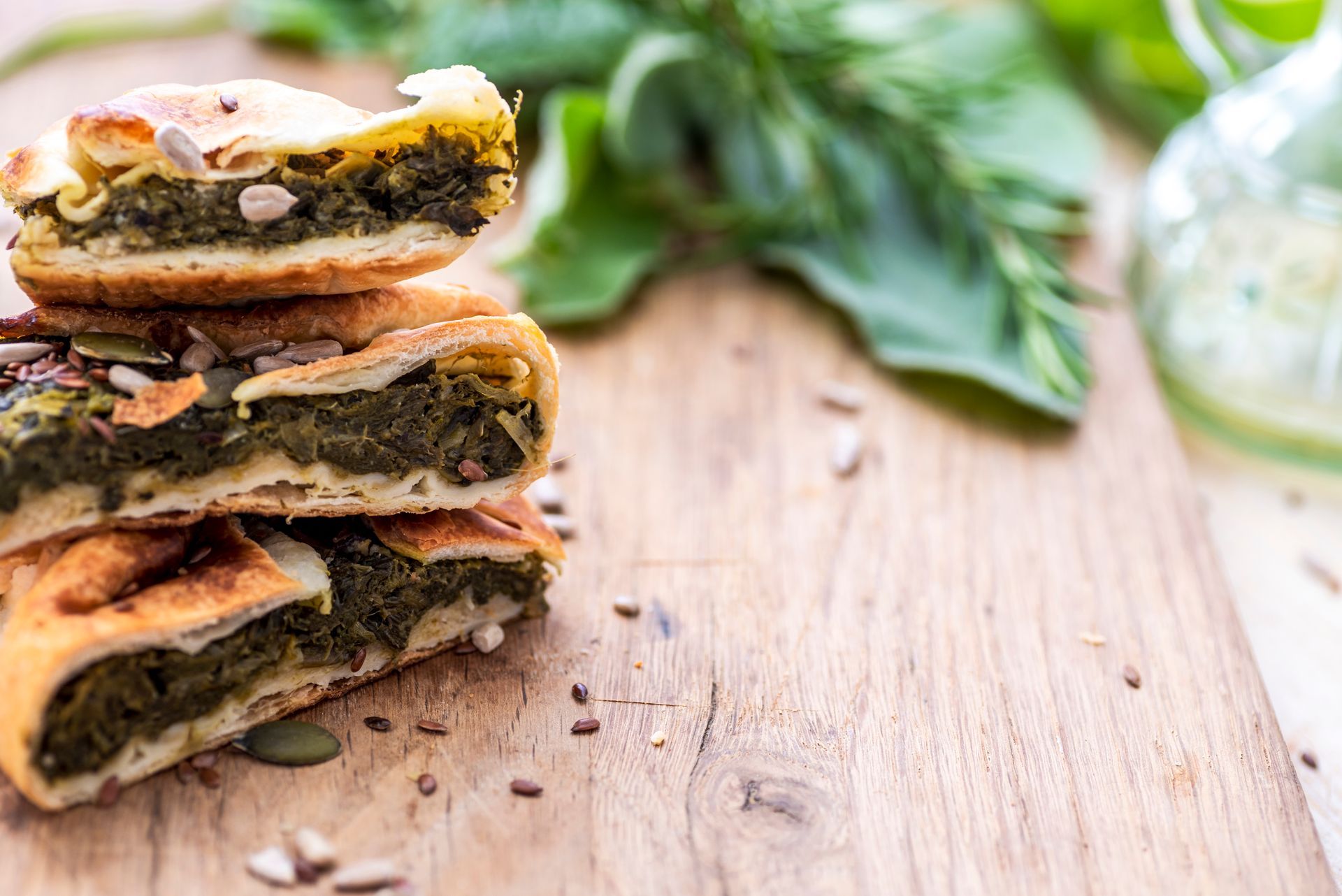 Fette di torta salata con ripieno verde, guarnite con semi, disposte su un tagliere di legno con del verde.
