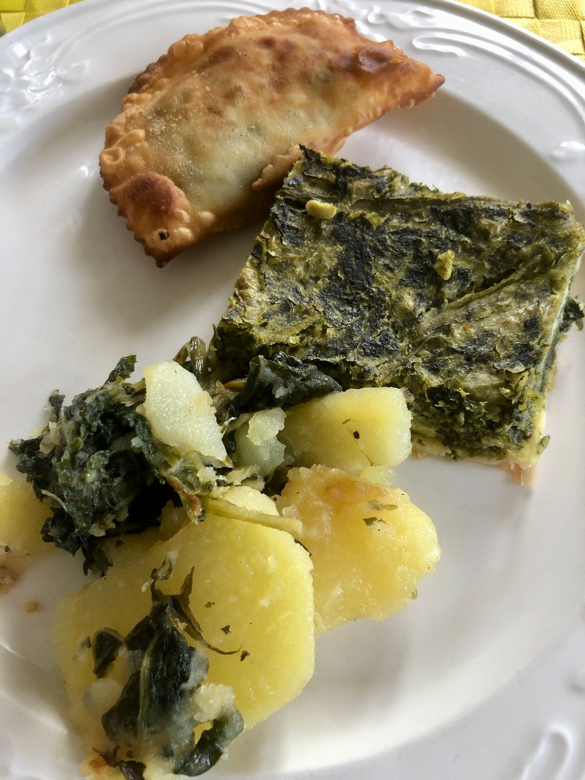 Piatto di cibo: un'empanada, una torta di spinaci e uova e patate con verdure.