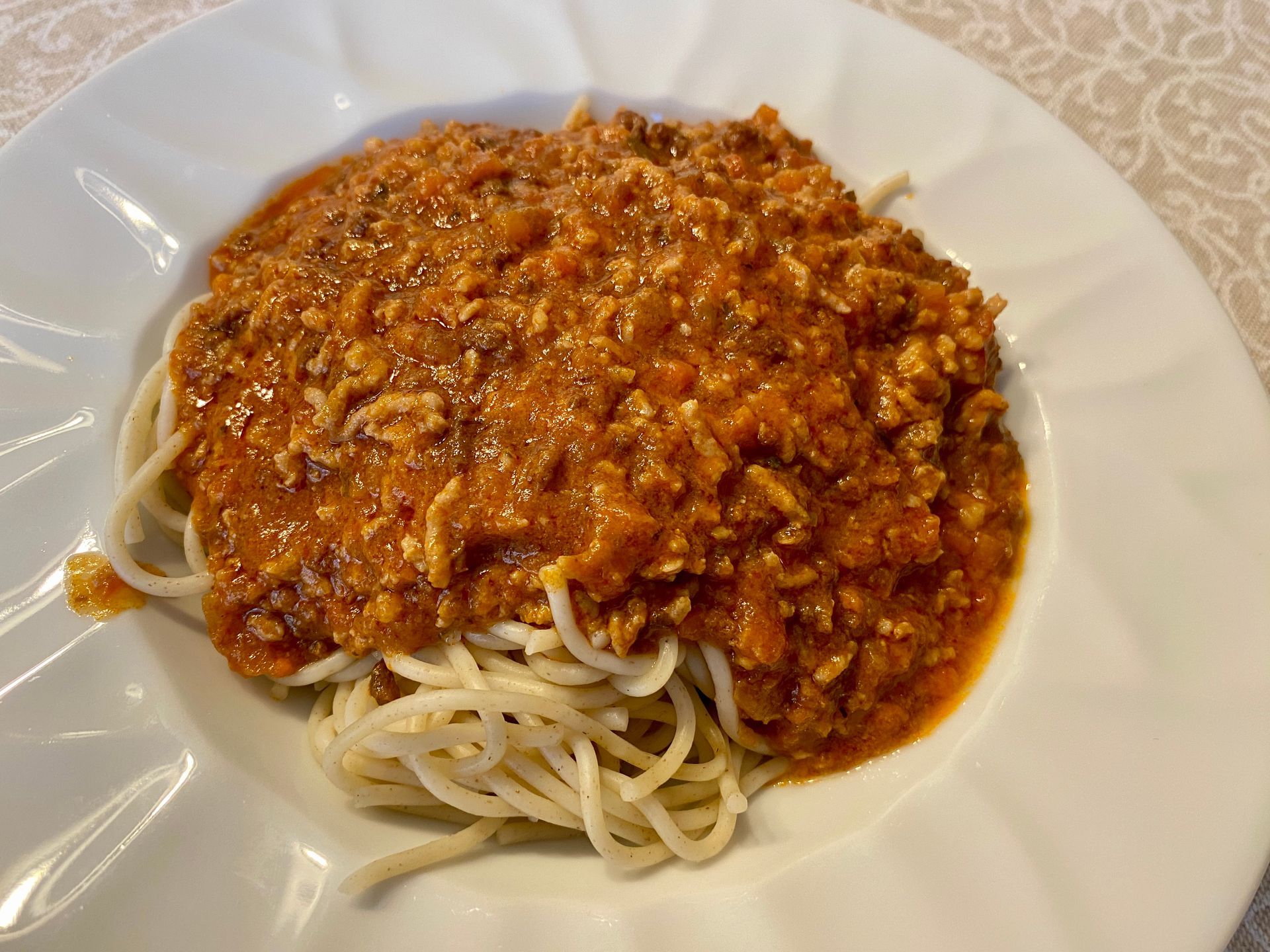 Spaghetti al ragù in una ciotola bianca. La salsa rosso-arancio ricopre gli spaghetti.
