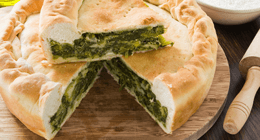 Torta salata di spinaci con una porzione tagliata a fette, su un tagliere di legno.