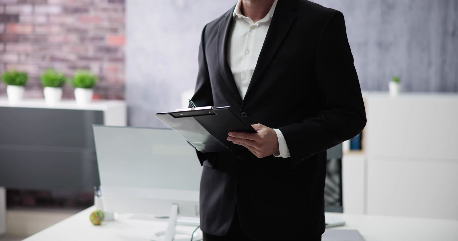 A man in a suit is holding a clipboard in an office.