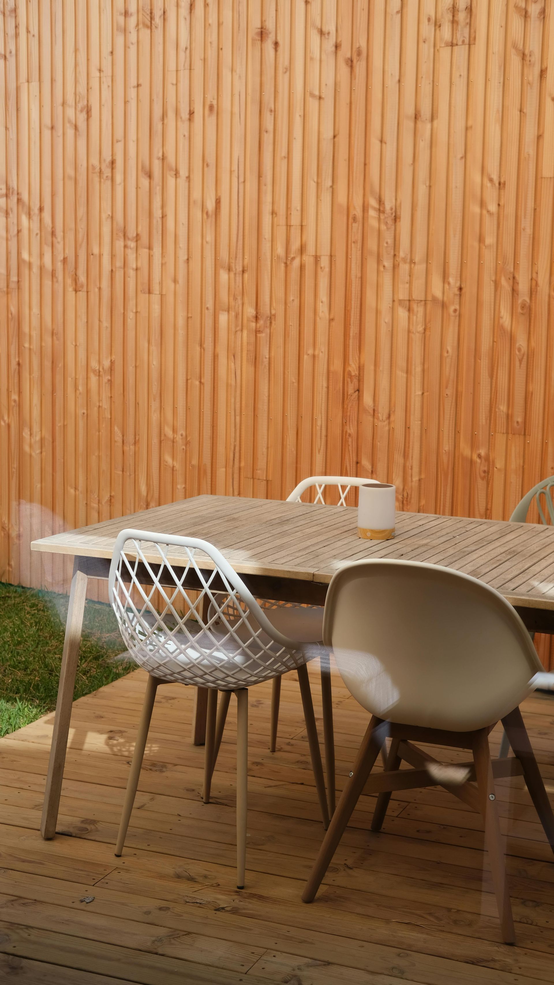 Outdoor patio dining table with chairs on a wooden deck beside a vertical wood fence