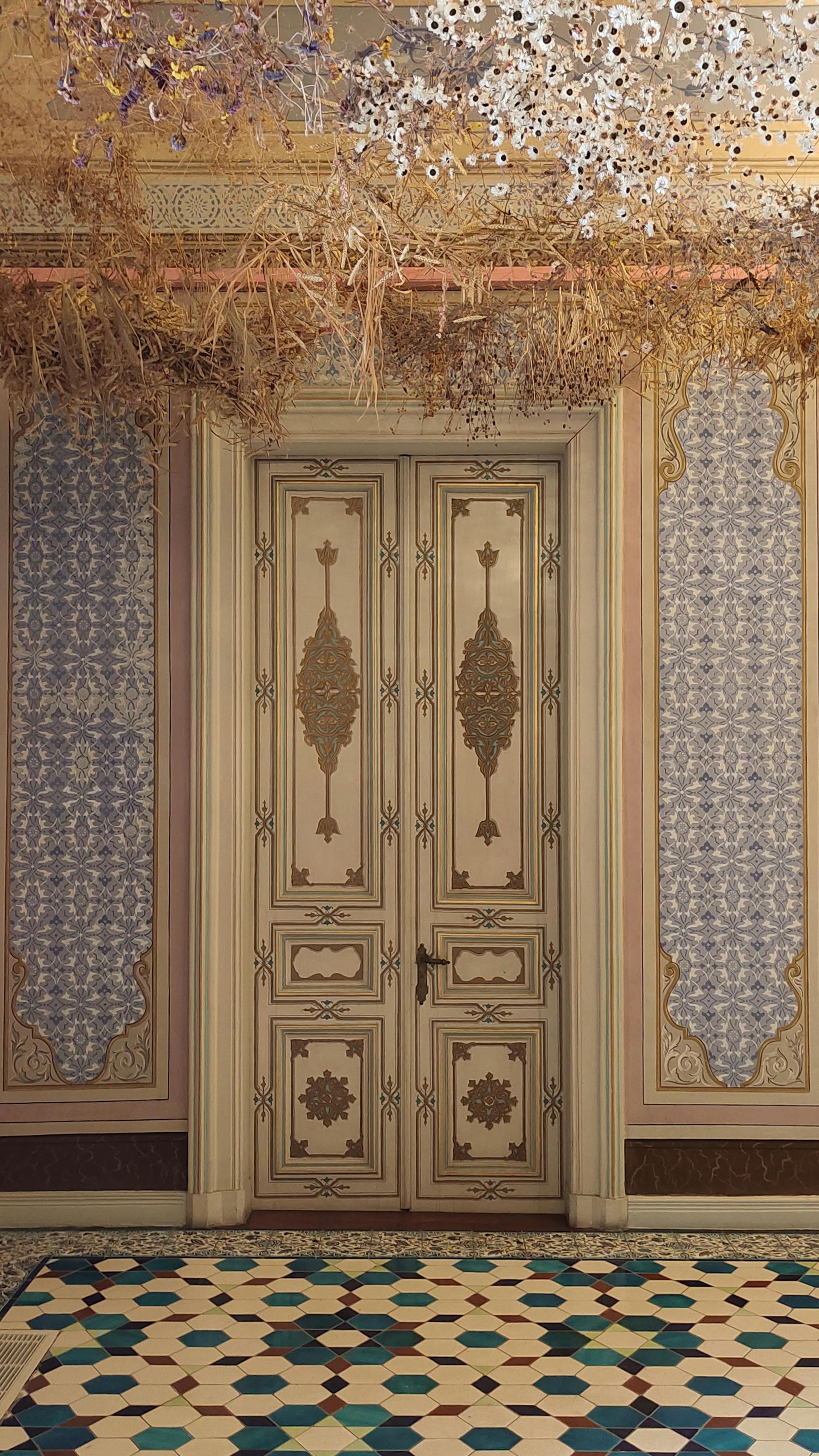 Ornate white double doors in a tiled hallway with blue patterned wall panels and a mosaic floor