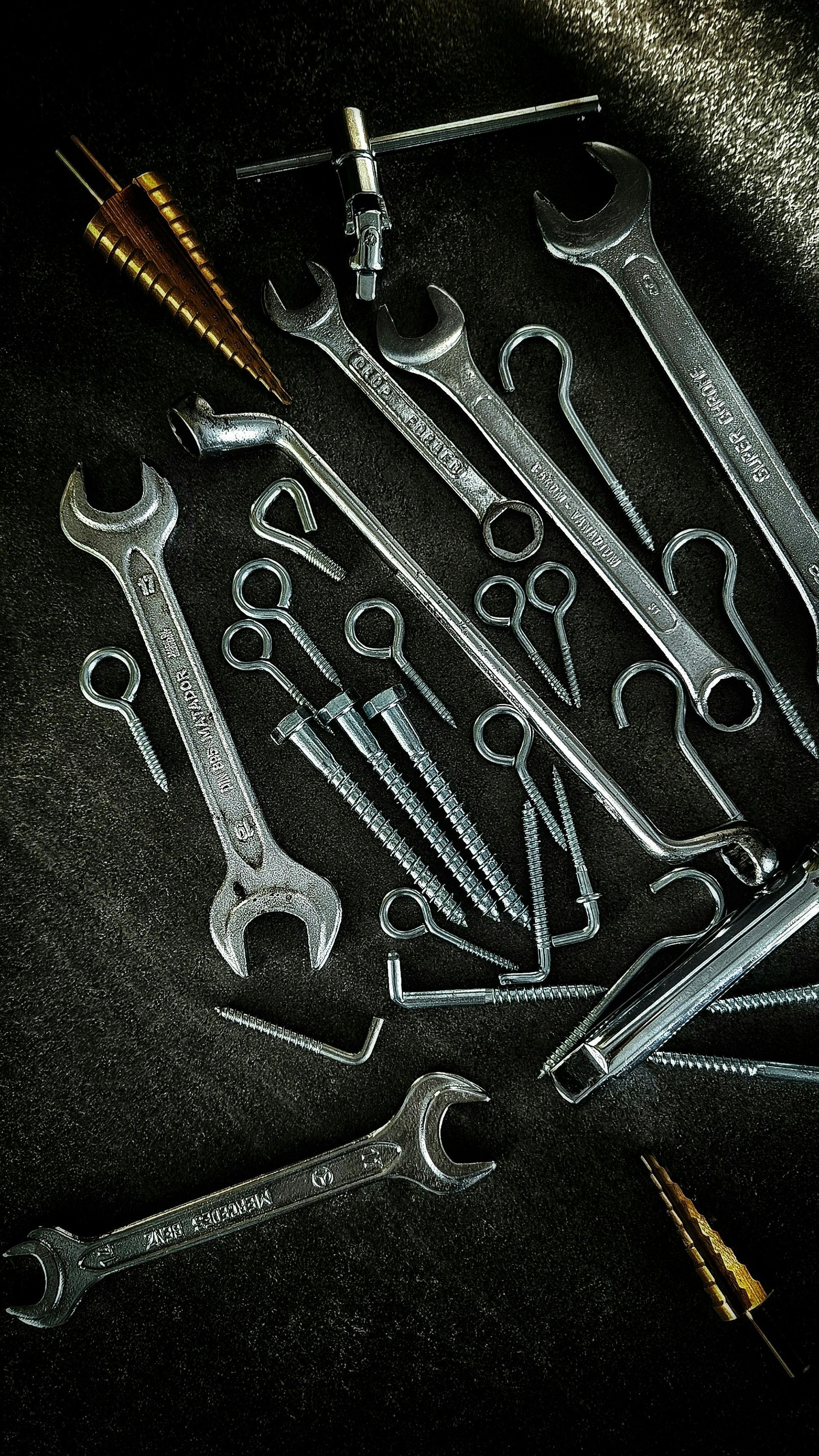 Assorted metal wrenches and hand tools arranged on a dark textured surface.