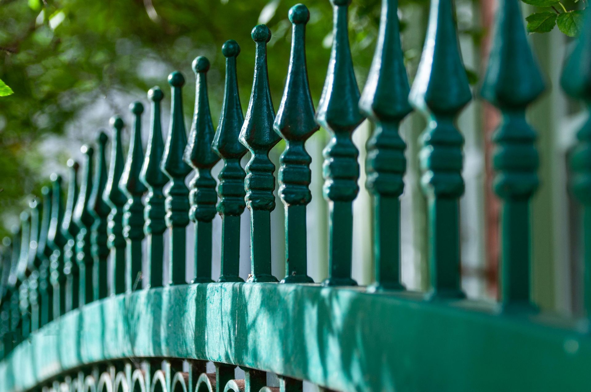 Green wrought-iron fence with pointed finials against a blurred leafy background