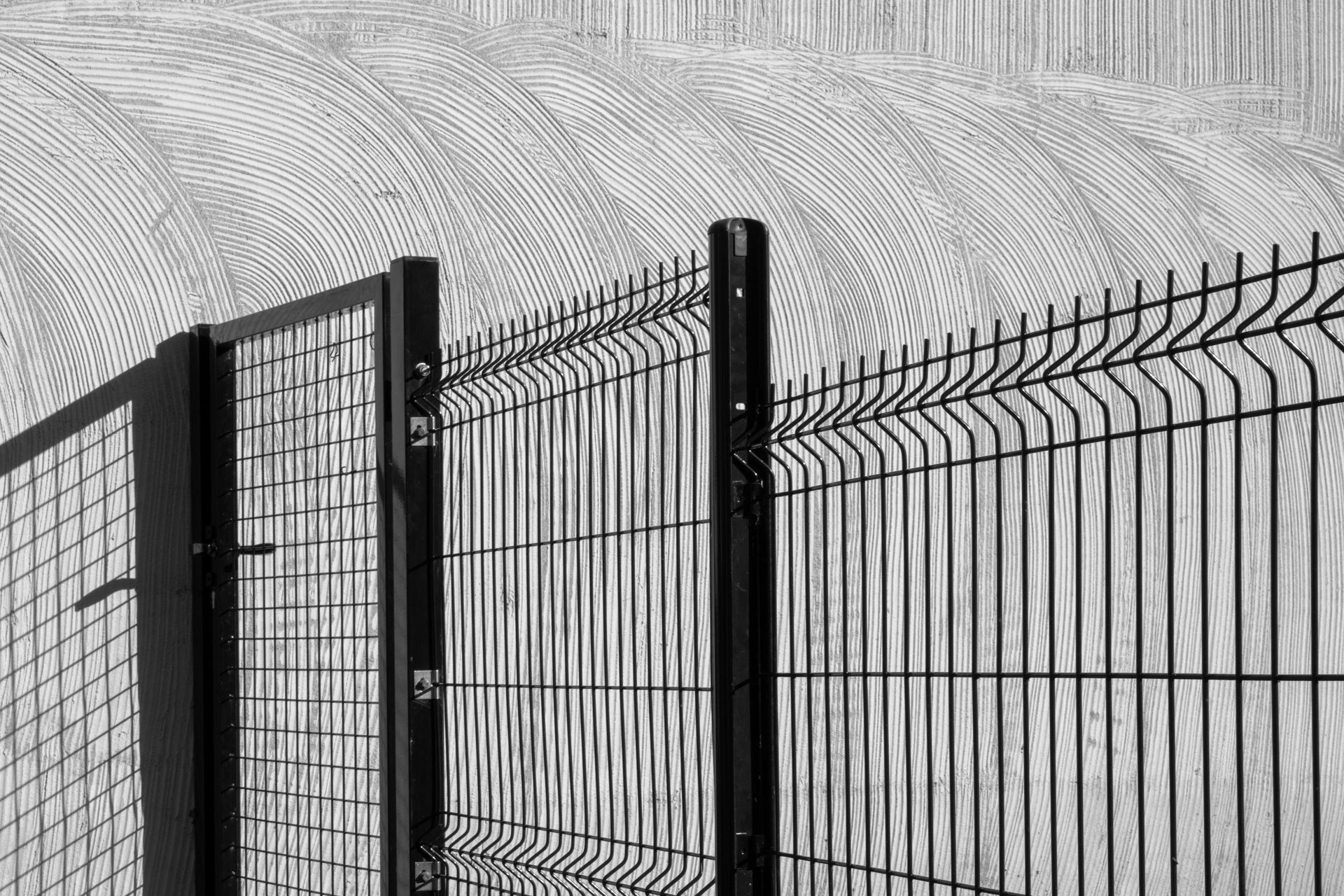 Black metal fence with curved spikes in front of a textured gray wall