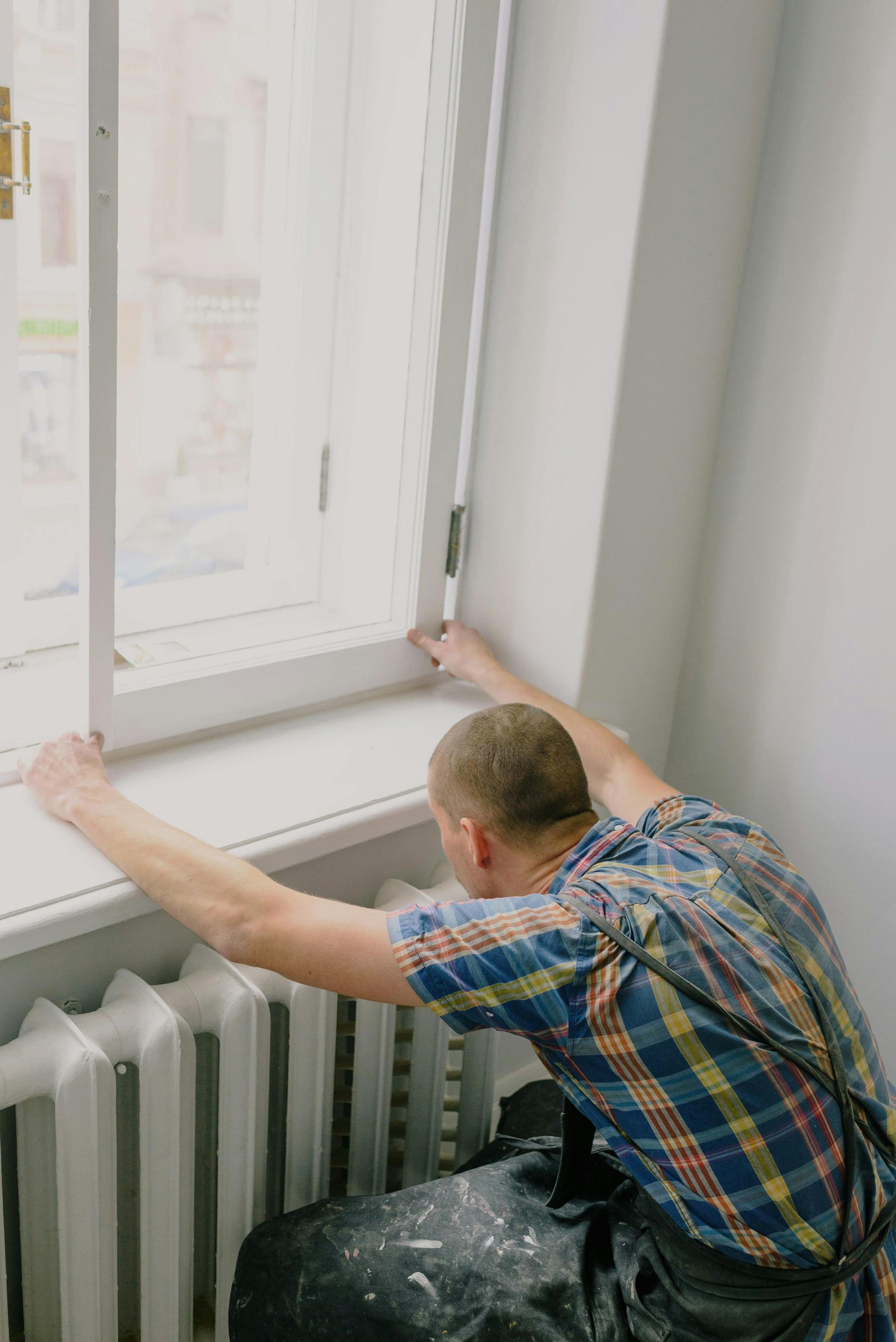 Worker adjusting a window frame beside a radiator in a bright room