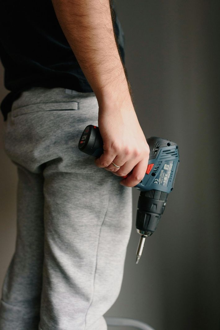 Person holding a gray power drill at their side against a dark background