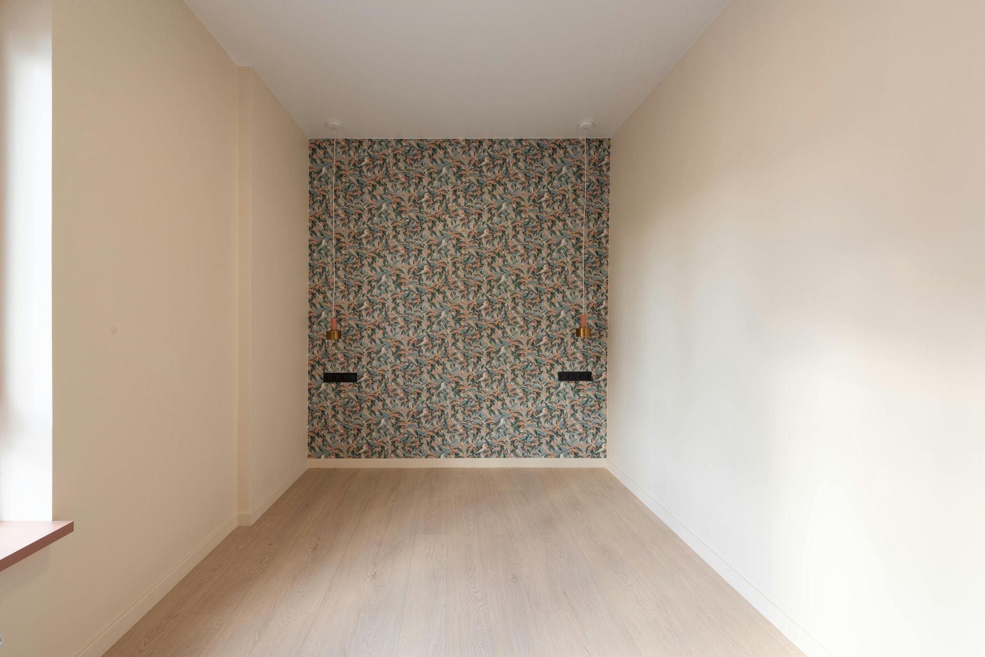 Empty beige room with light wood floor and patterned accent wall at the far end
