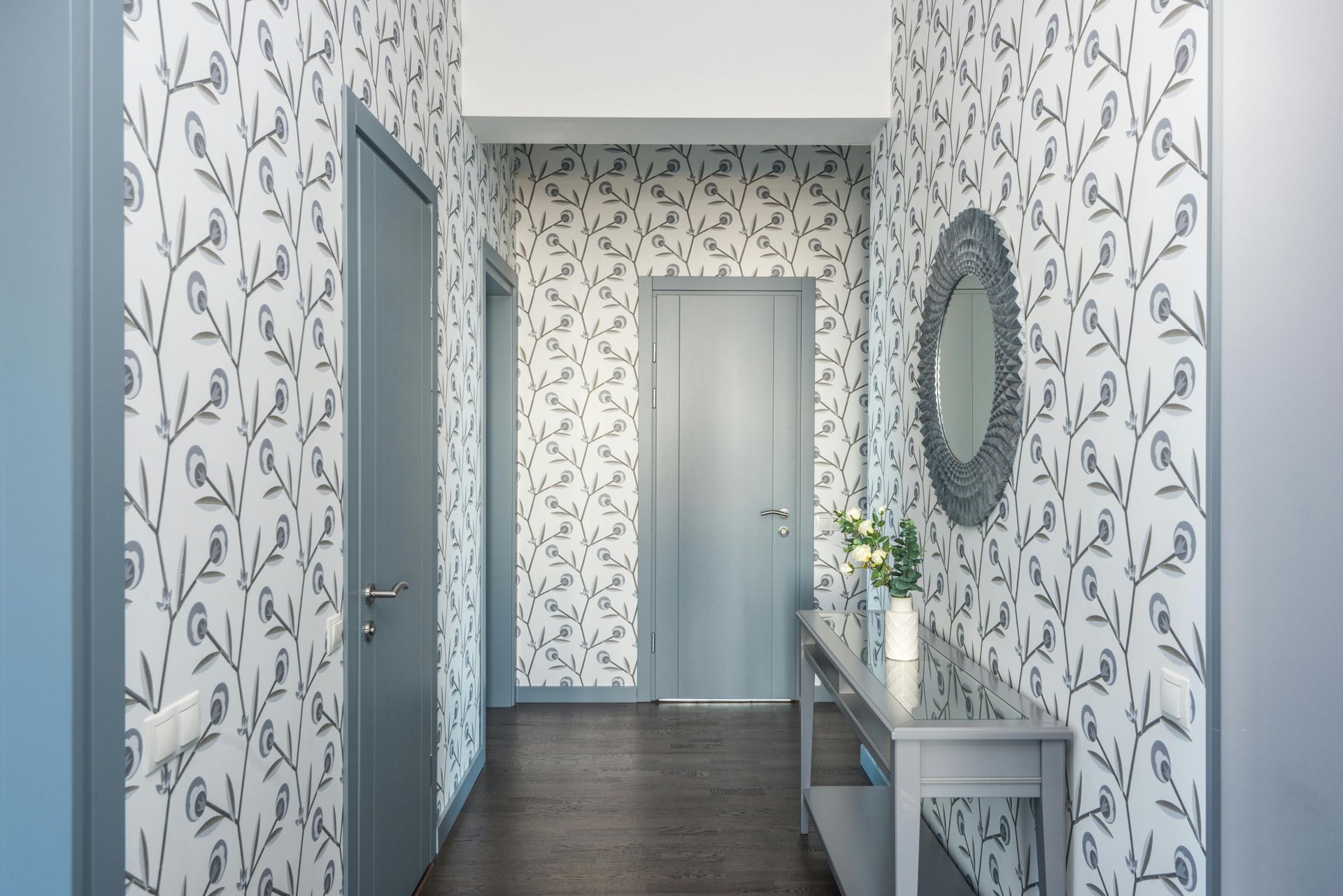 Modern hallway with floral wallpaper, blue doors, dark wood floor, and a console table with mirror and flowers