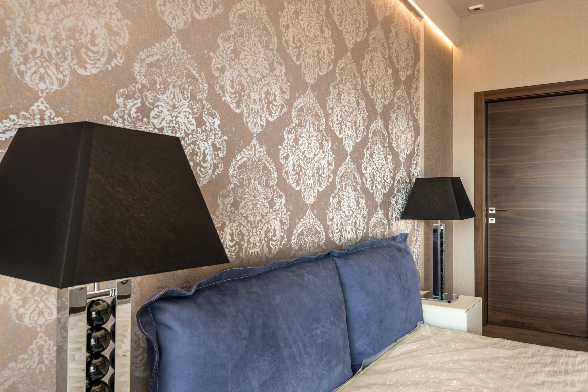 Modern bedroom with blue headboard, patterned wallpaper, black lamps, and a wooden door