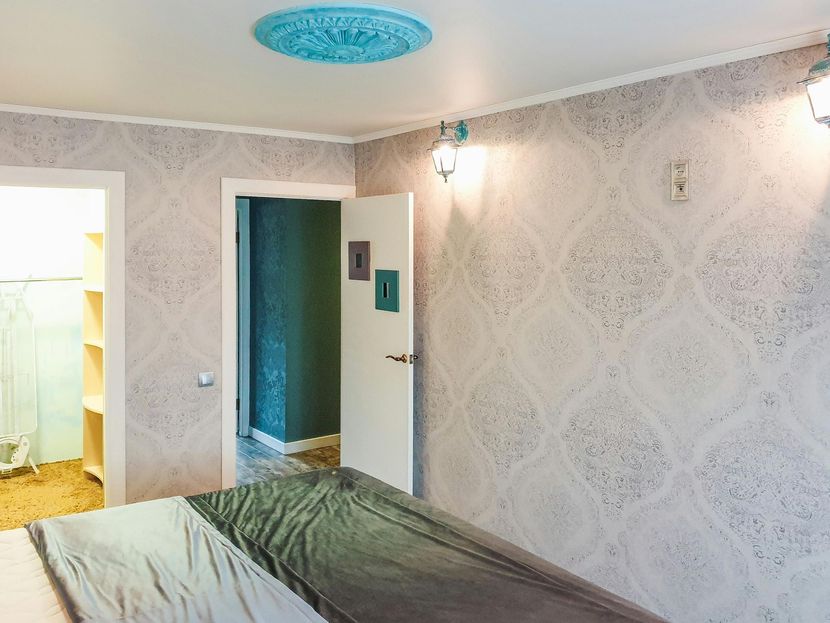 Bedroom with patterned wallpaper, blue ceiling light, open door, and teal-accented doorway
