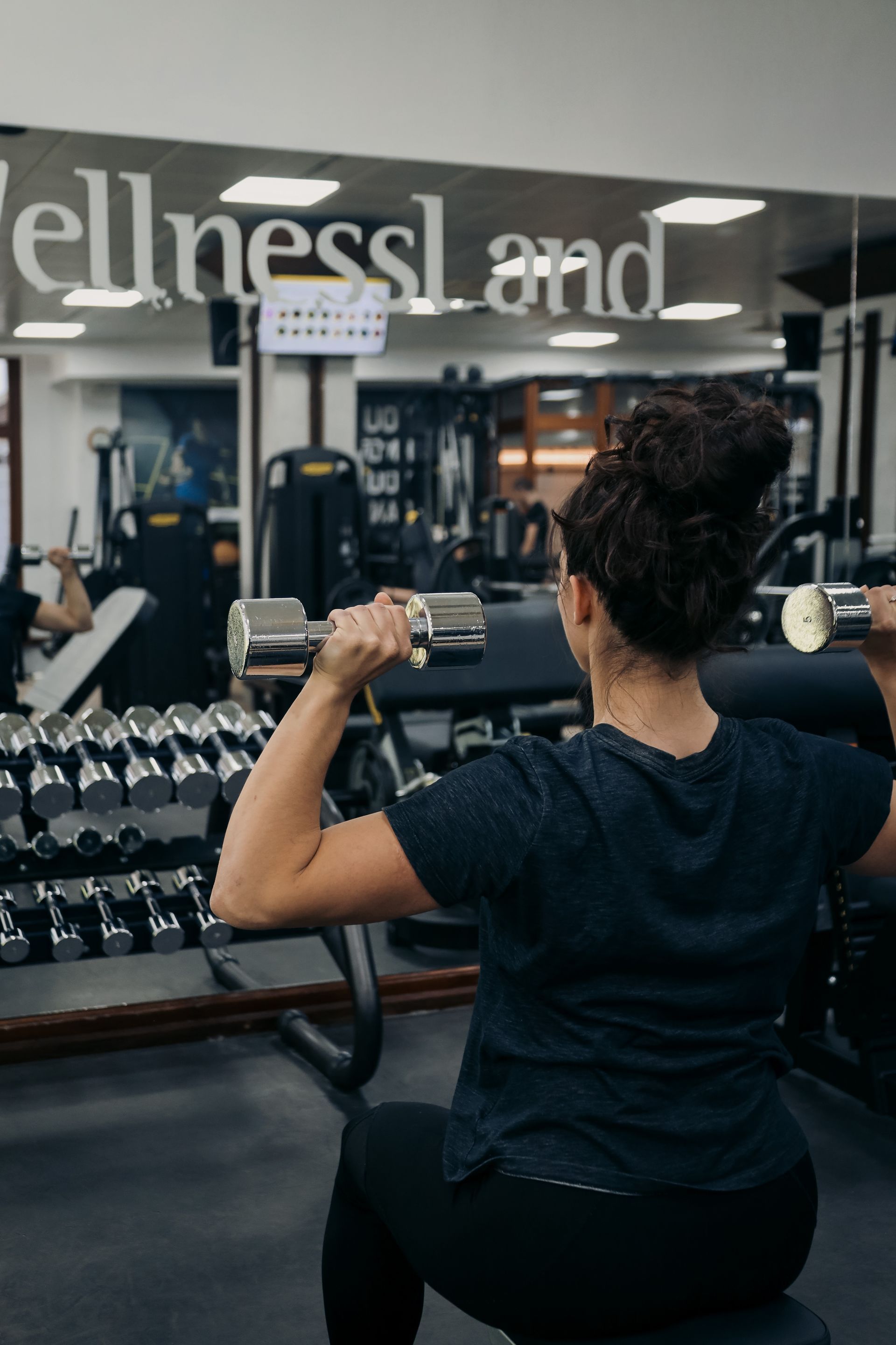 a woman is lifting dumbbells in a gym in front of a sign that says wellnessland