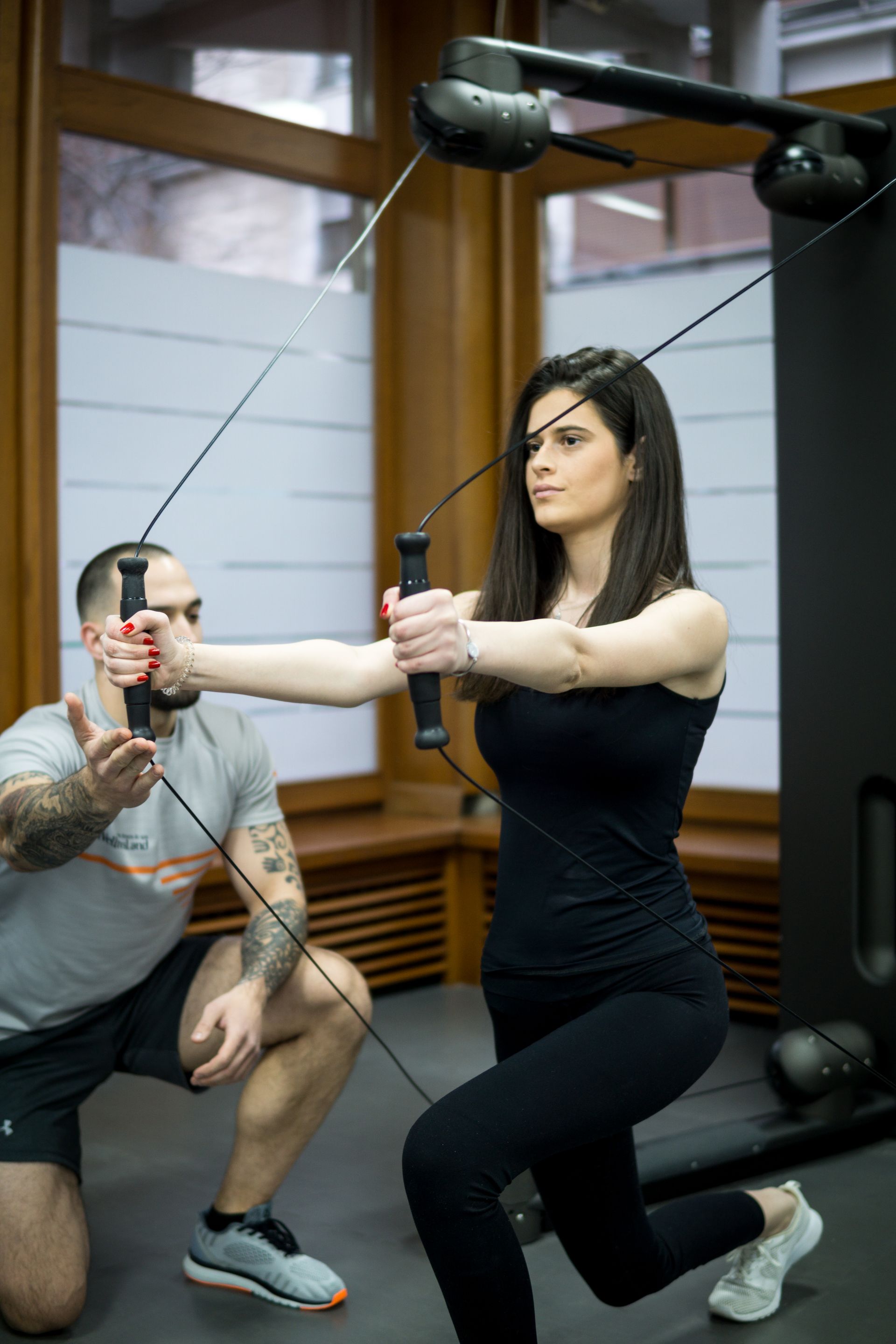 a man is helping a woman do exercises on a machine in a gym .