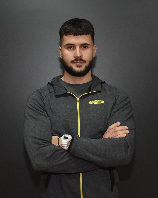 a man wearing a grey jacket with a yellow zipper has his arms crossed