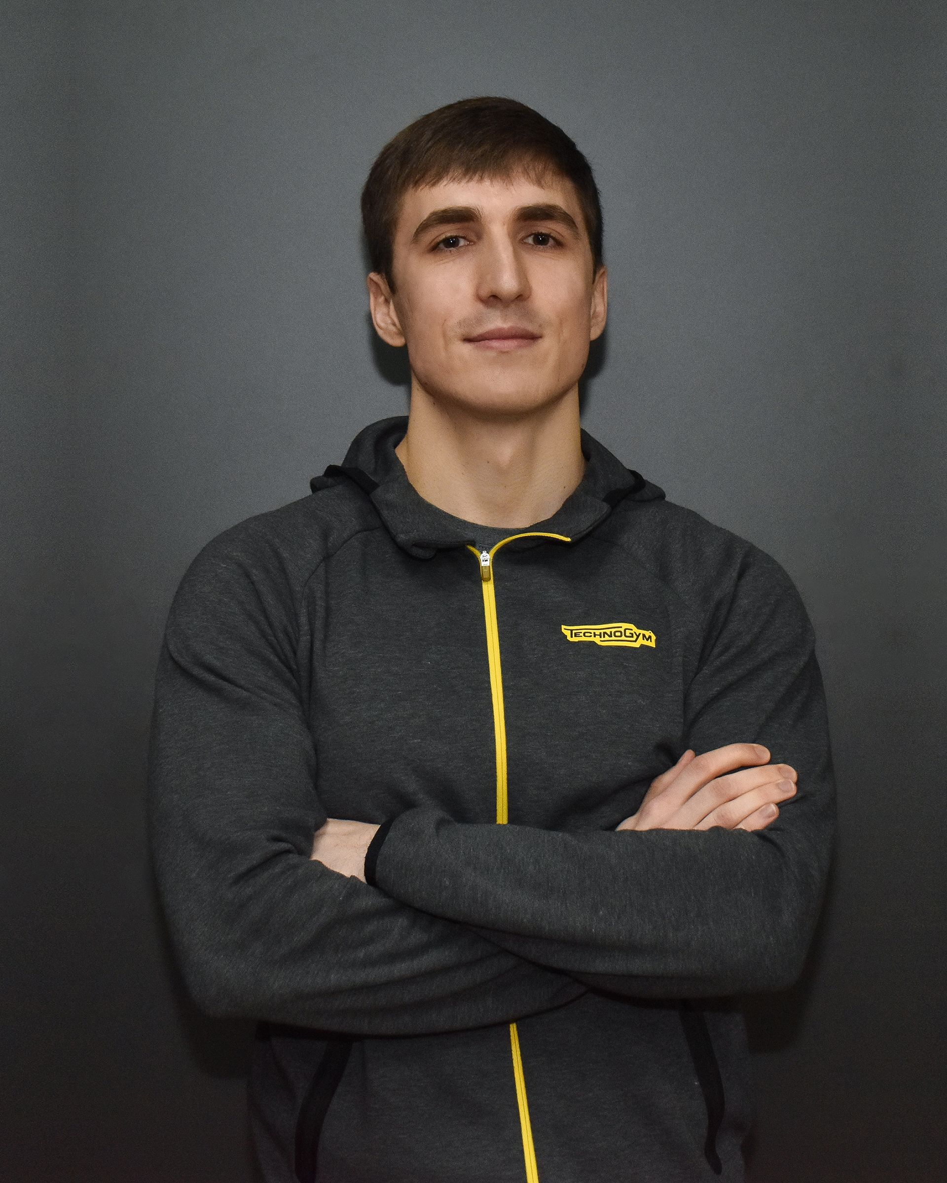a man wearing a grey jacket with a yellow zipper has his arms crossed