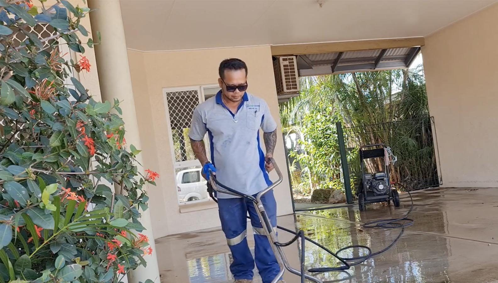 A Man is Cleaning the Floor of a House With a Hose — Bali Green Cleaners in Winnellie, NT
