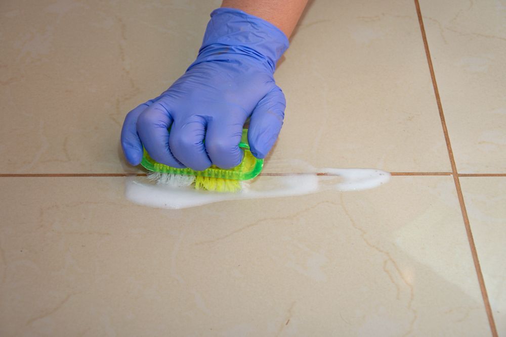 A Person Wearing Gloves is Cleaning a Tile Floor With a Sponge — Bali Green Cleaners in Winnellie, NT