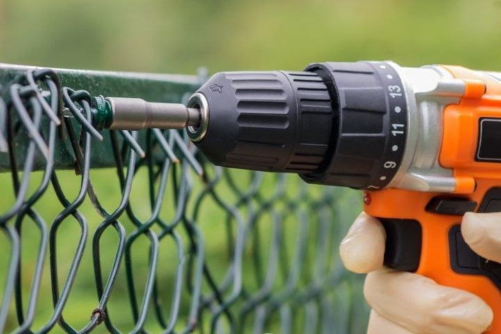 Orange power drill used to attach something to a green chain-link fence.