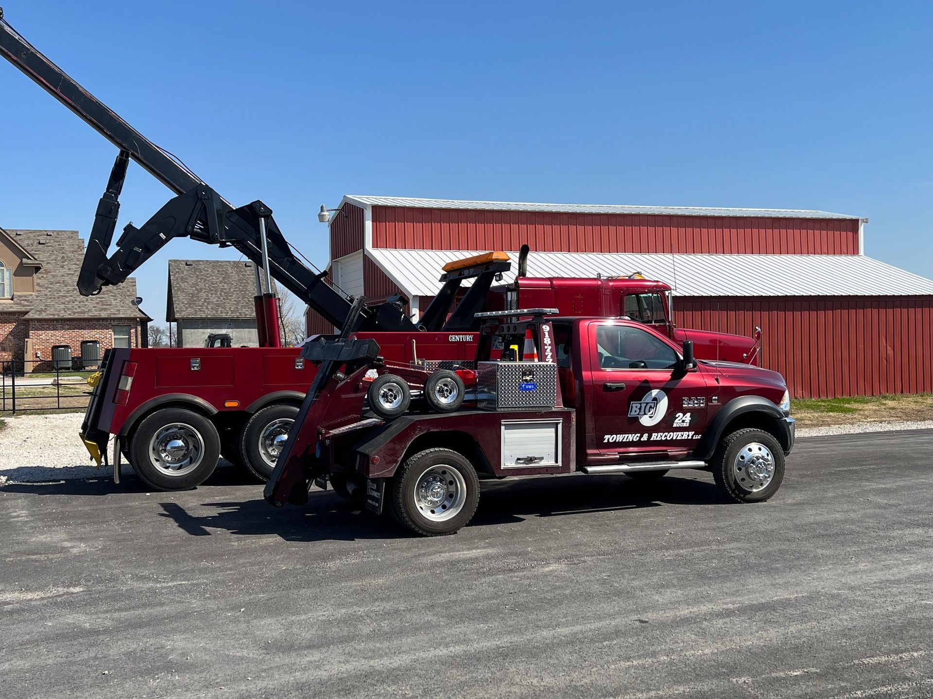 Red tow truck, parked on pavement in front of a red barn.