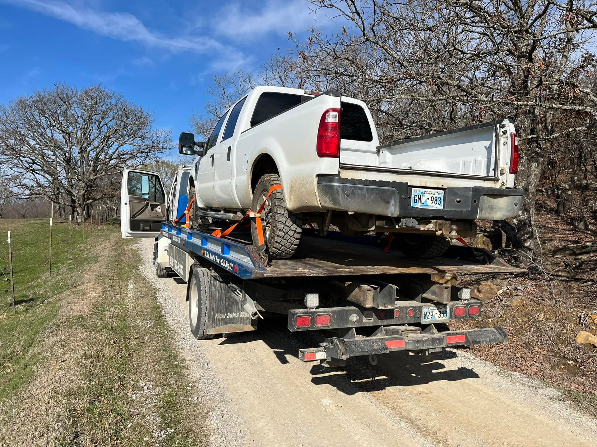 White truck being towed on a tow truck along a dirt road.