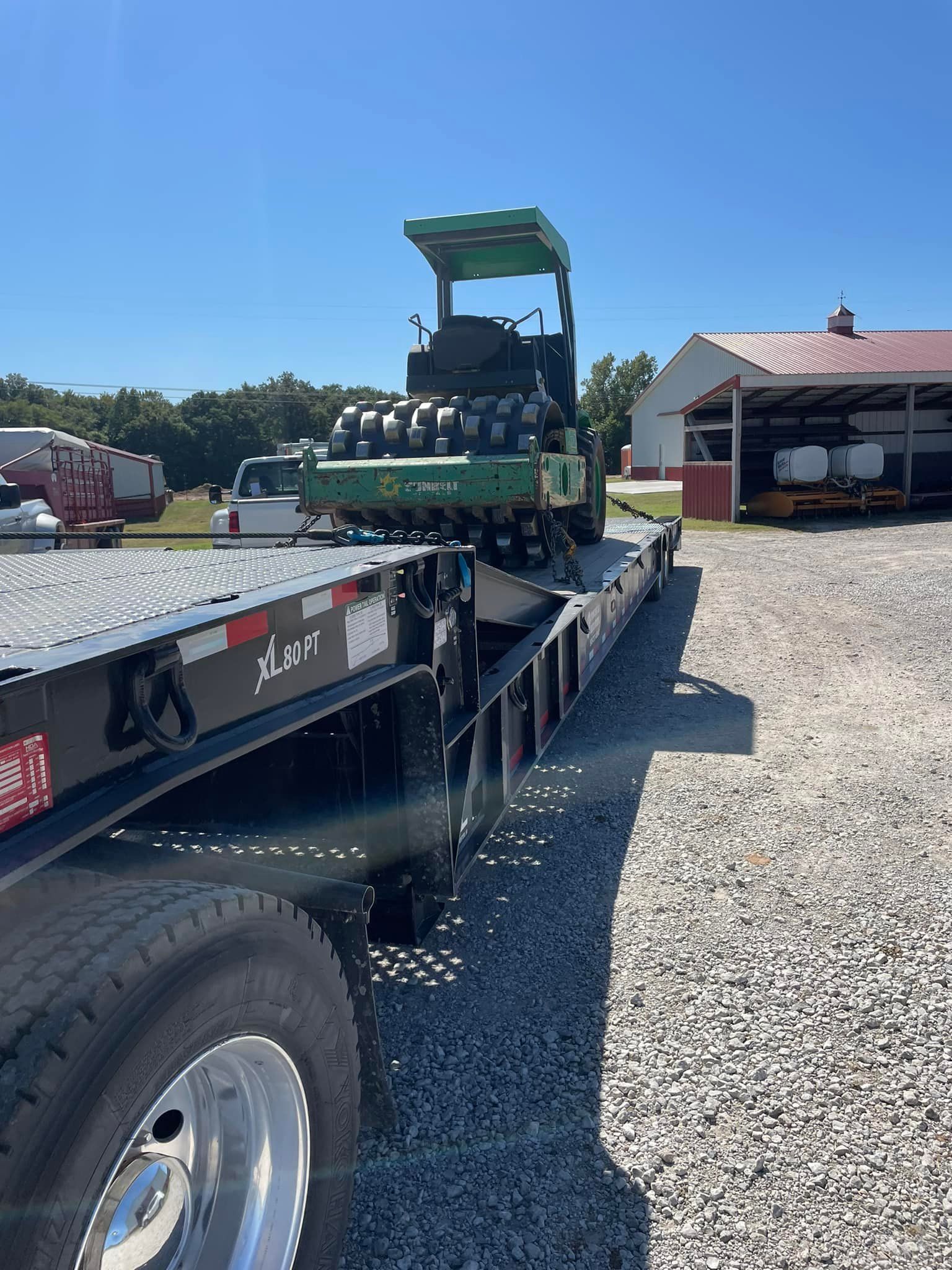 John Deere tractor on a black flatbed trailer in front of a white building on a sunny day.