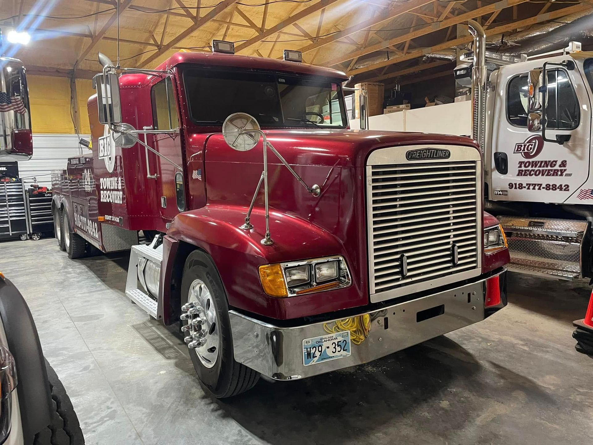 A burgundy tow truck in a garage. It has chrome features, license plate, and is parked in a garage.