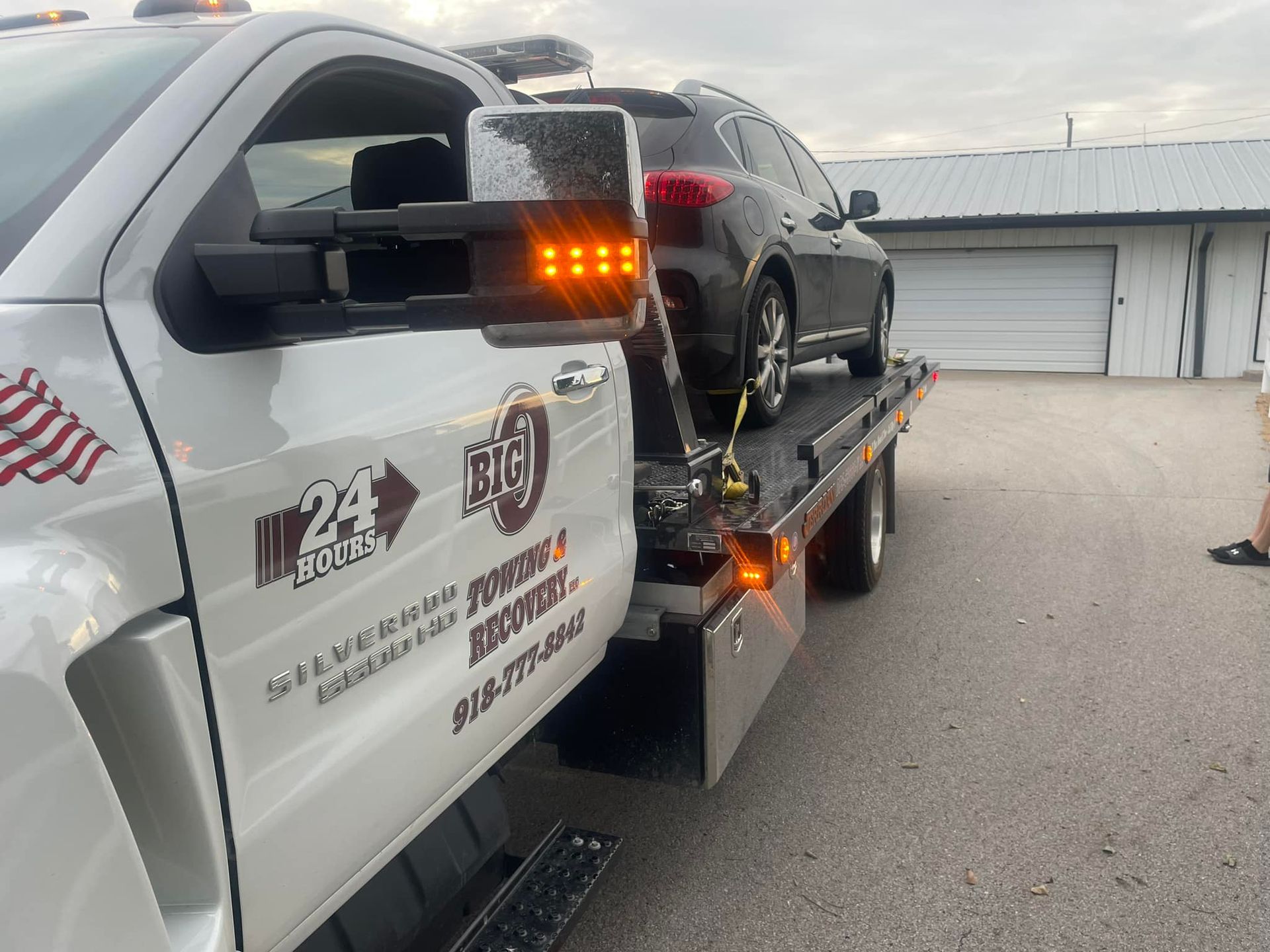 Tow truck hauling a black SUV; the truck has orange lights.