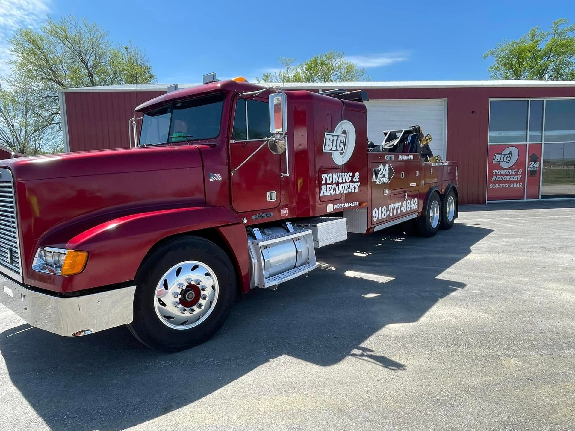 Red tow truck parked in front of a red building on a sunny day.