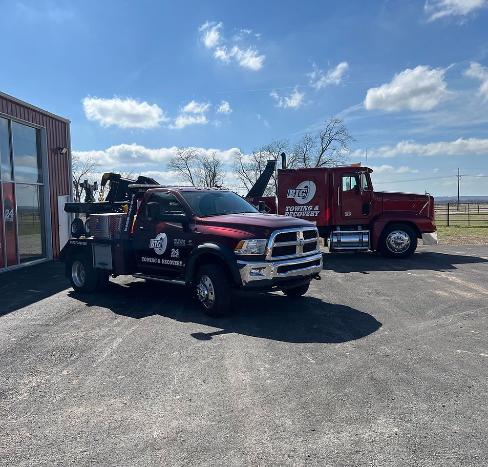 Two tow trucks, one burgundy and one red, parked outside under a blue sky.