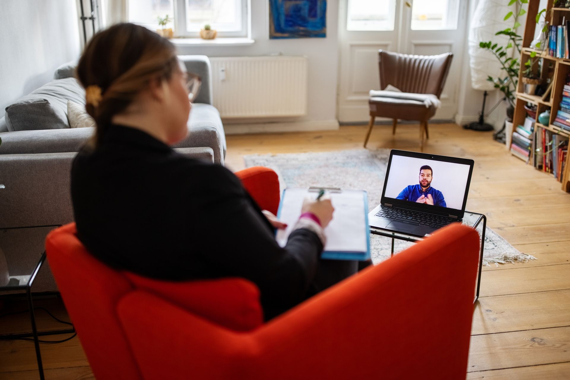 A woman is sitting in a red chair in front of a laptop computer.