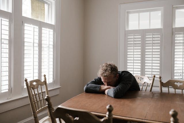 A man is sitting at a table with his head on his hands.