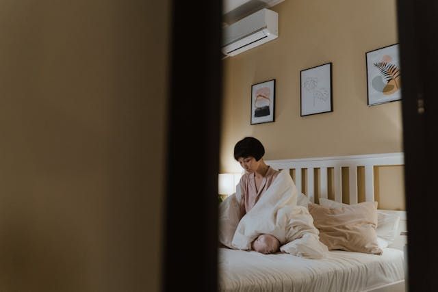 A woman is sitting on a bed covered in a blanket.