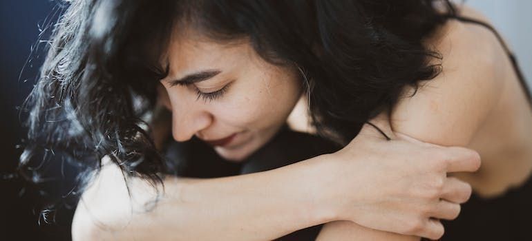 A woman is hugging herself with her eyes closed.